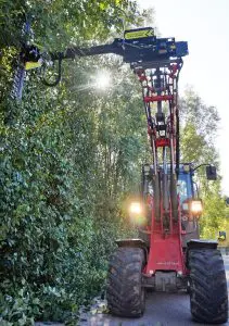 Traktor mit einer GreenTec Heckenpflegemaschine schneidet Hecke auf einer Straße in Henndorf.