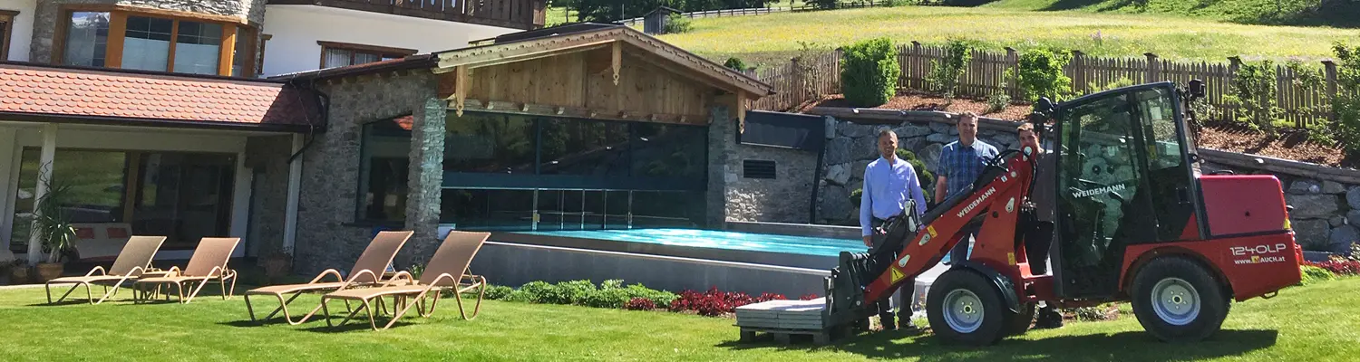 Zwei Männer stehen neben einer roten Weidemann 1240LP vor einem modernen Haus mit Pool im Garten.