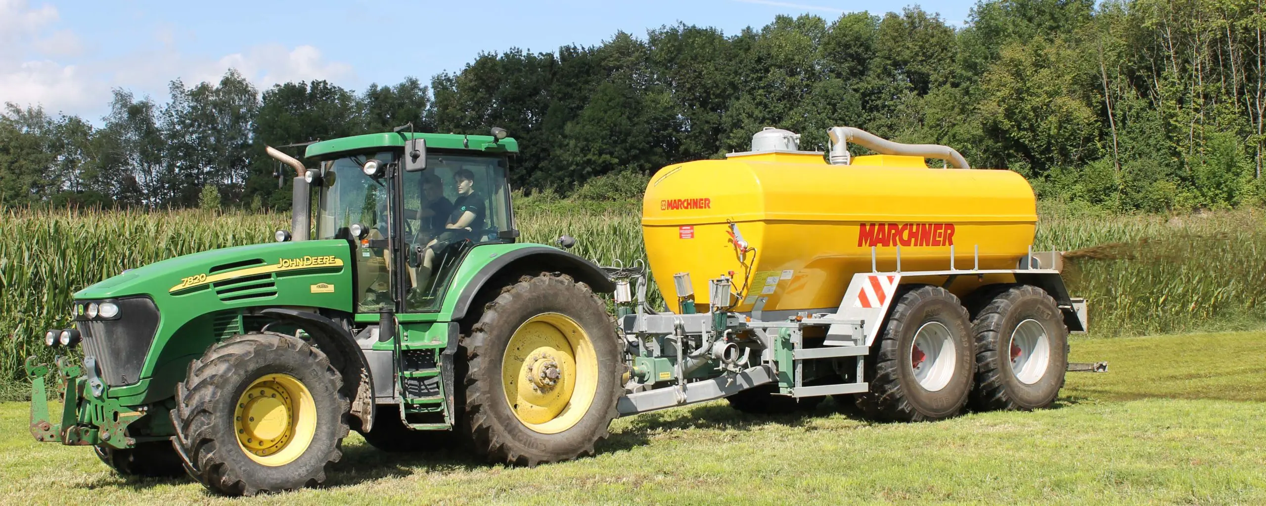 Grüner John Deere 7830 Traktor mit gelbem Marchner-Güllefass auf einem Feld.