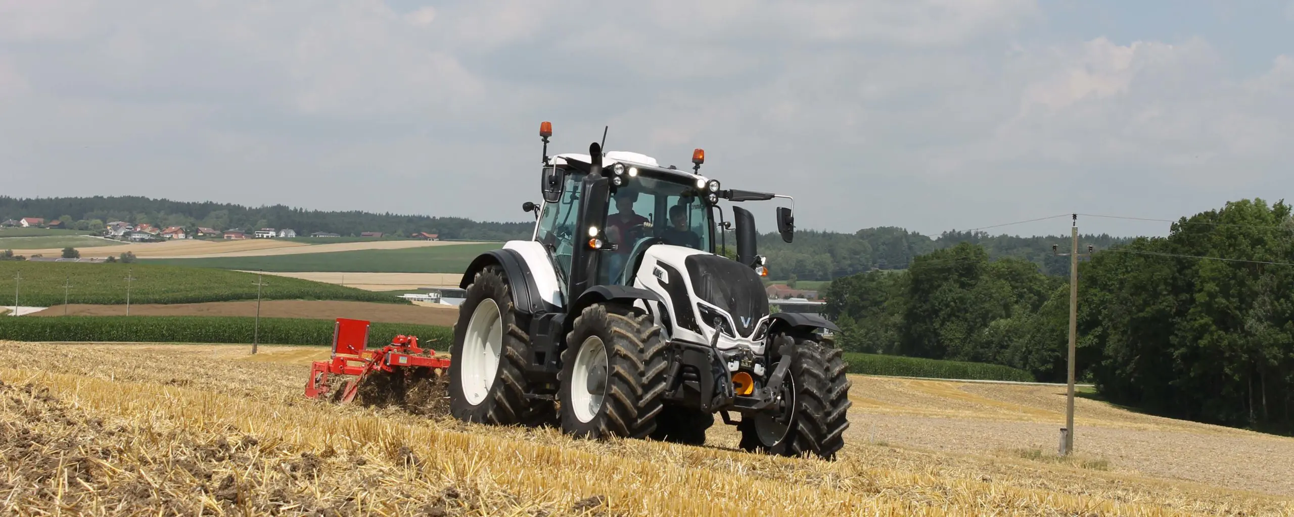 Ein Traktor fährt über ein abgeerntetes Feld vor ländlicher Kulisse.