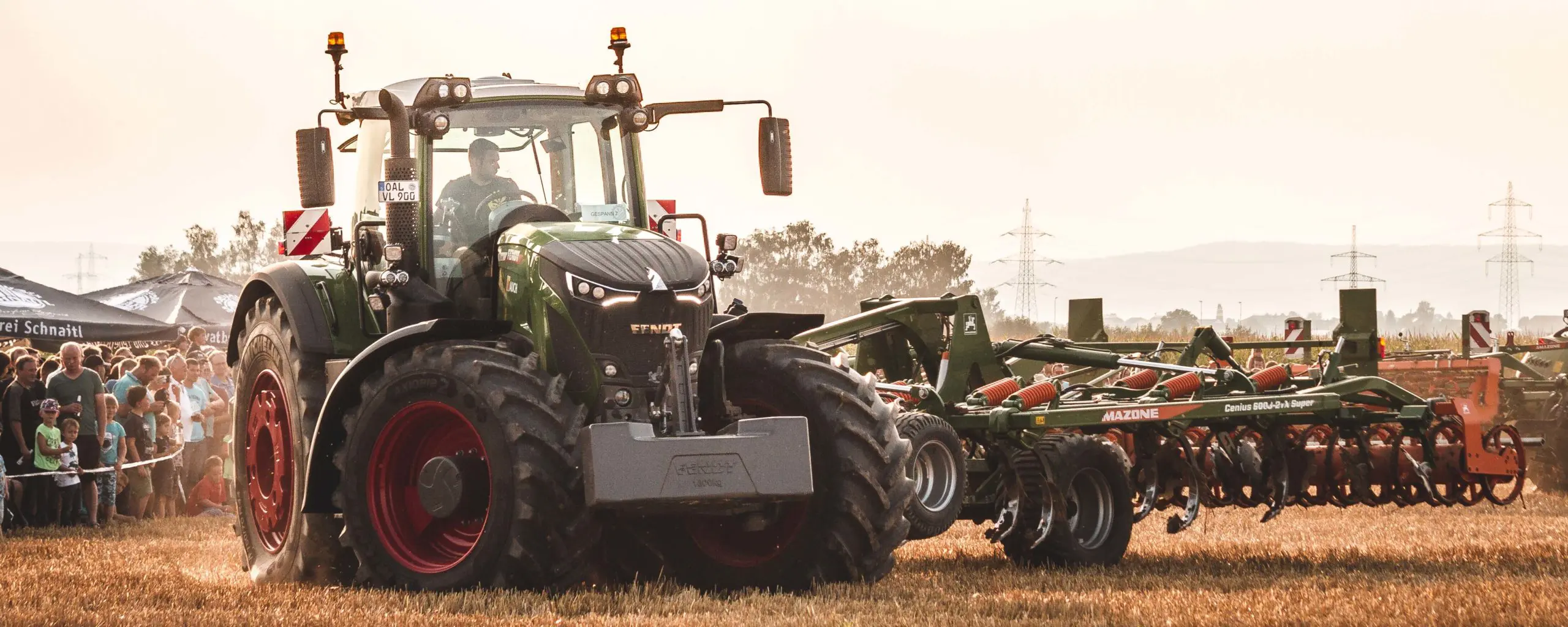 Ein Fendt-Traktor mit einem Amazone-Gerät im Einsatz auf einem Feld, umgeben von einer Menschenmenge.