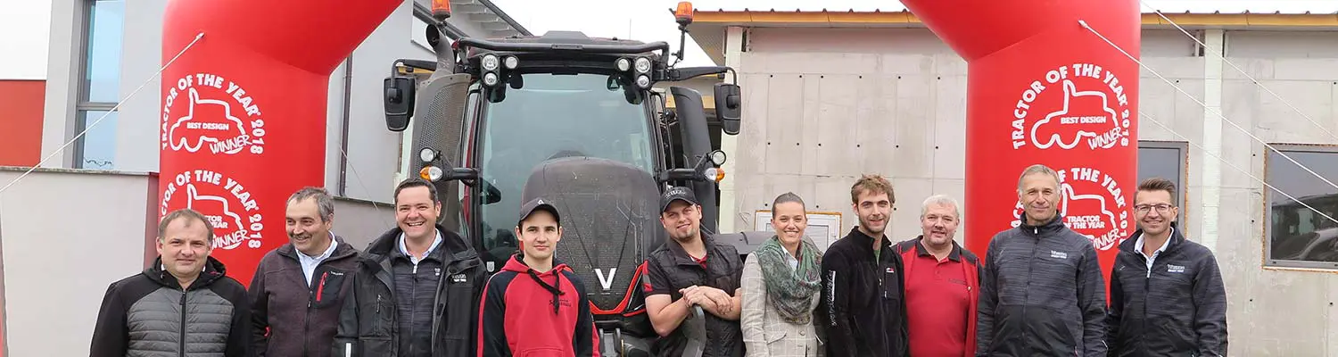 Gruppe von Personen steht vor einem Valtra T254 Versu-Traktor neben zwei roten Tractor of the Year 2018-Bögen.