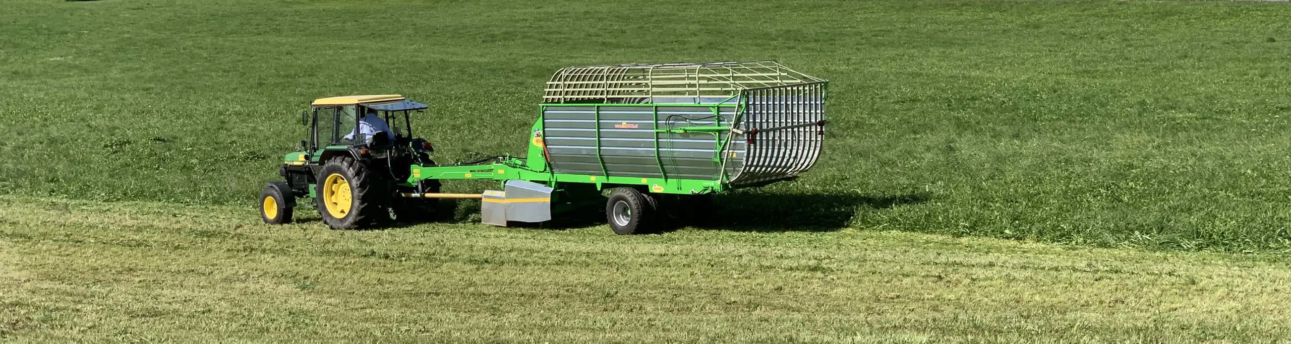 Traktor zieht einen grünen Bonino-Anhänger über eine Wiese.