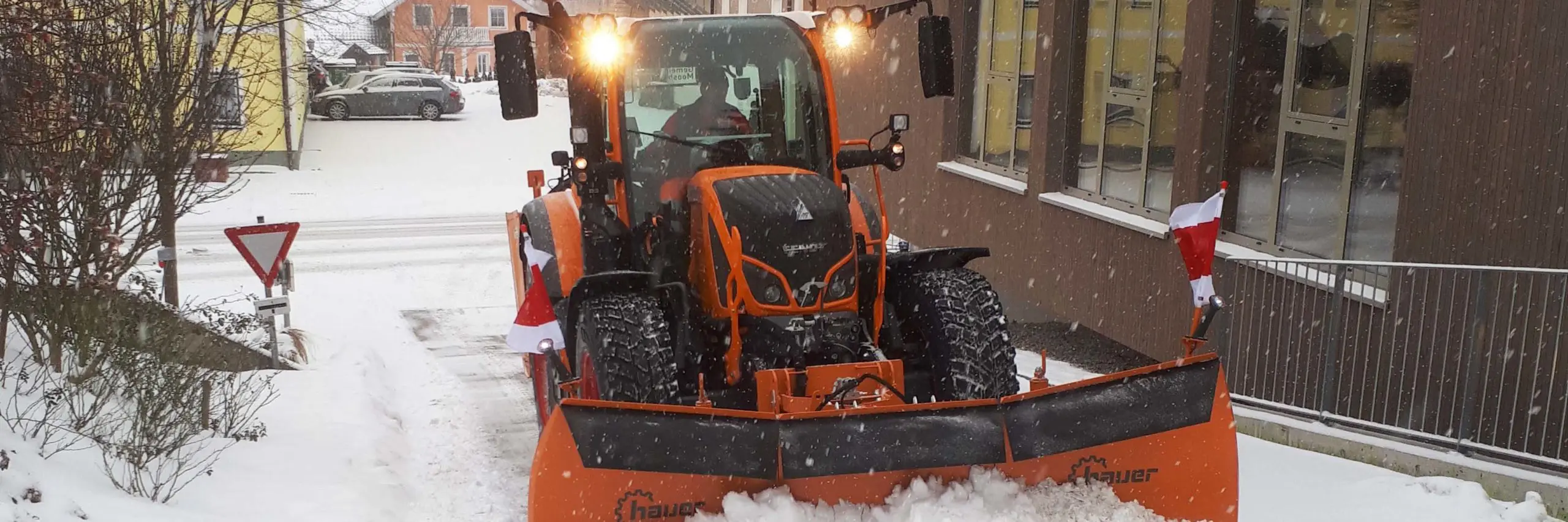 Ein Fendt 512 Traktor mit Schneepflug der Marke Hauer räumt eine verschneite Straße.