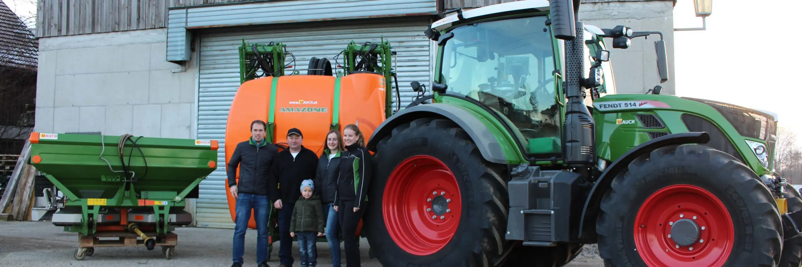 Eine Familie steht vor einem Fendt 514 Traktor und Amazone Sämaschine neben einem Gebäude.