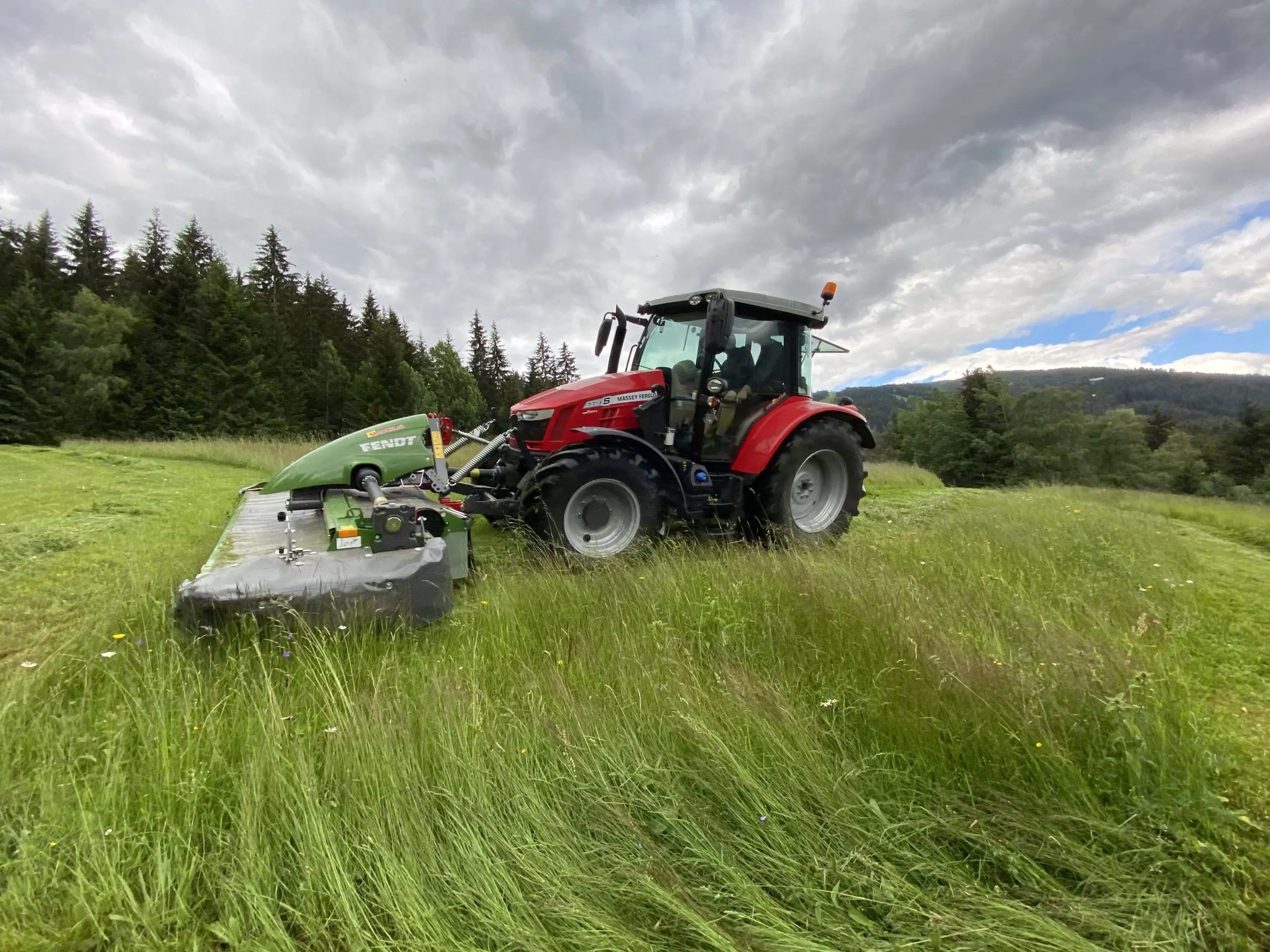 Roter Massey Ferguson Traktor mäht mit einem Fendt-Mähwerk eine Wiese.