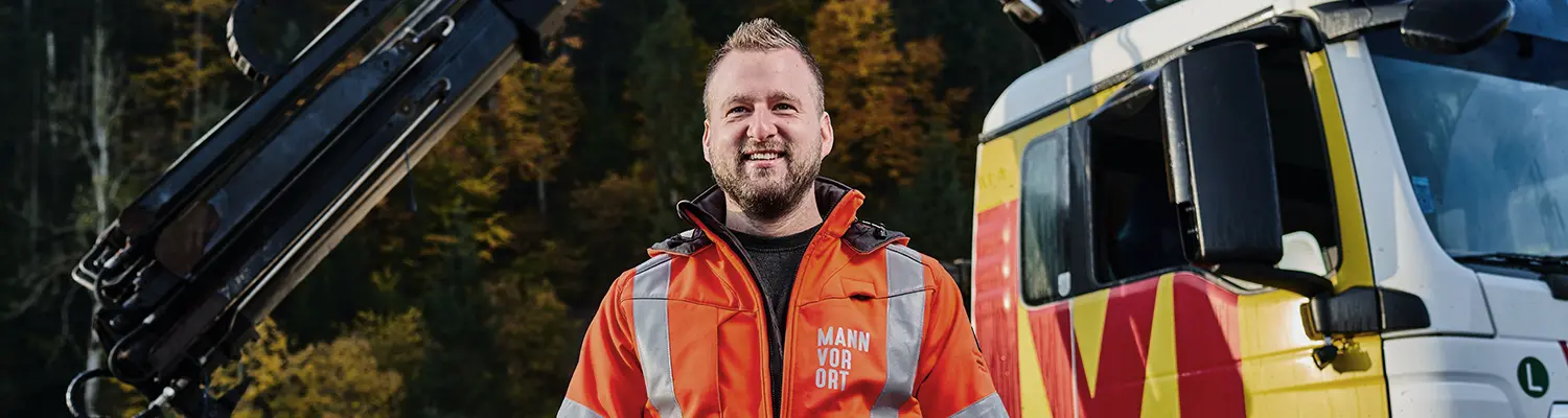 Ein Mann in einer Jacke mit der Aufschrift Mann vor Ort neben einem LKW.