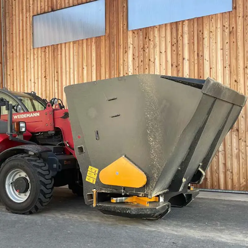 Ein Weidemann-Lader mit einem Emily-Multispreader steht vor einer Holzwand.