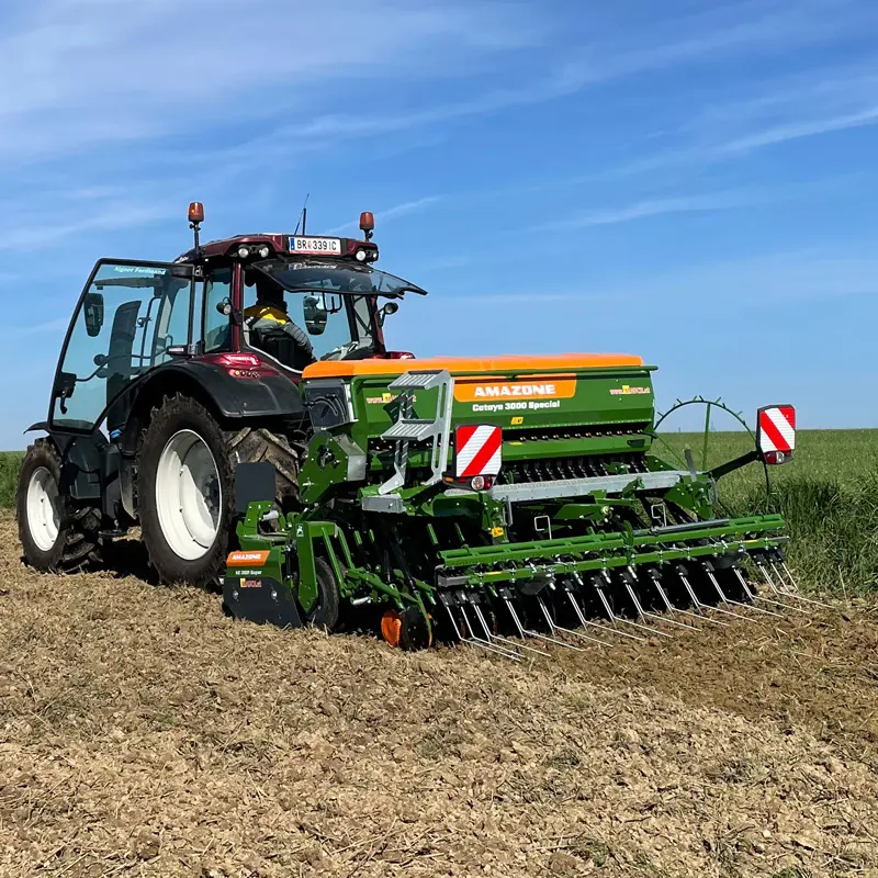 Ein Traktor der Marke Valtra N134 zieht eine Amazone Cataya 3000 Special Sämaschine auf einem Feld.