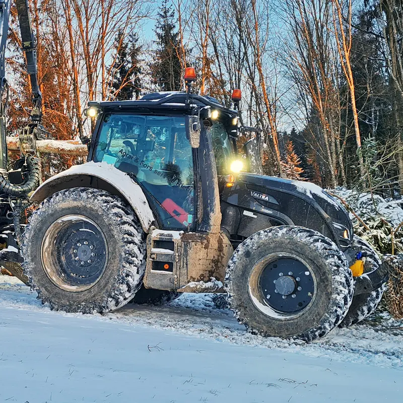 Ein Valtra N174 Traktor in einer verschneiten Waldlandschaft.