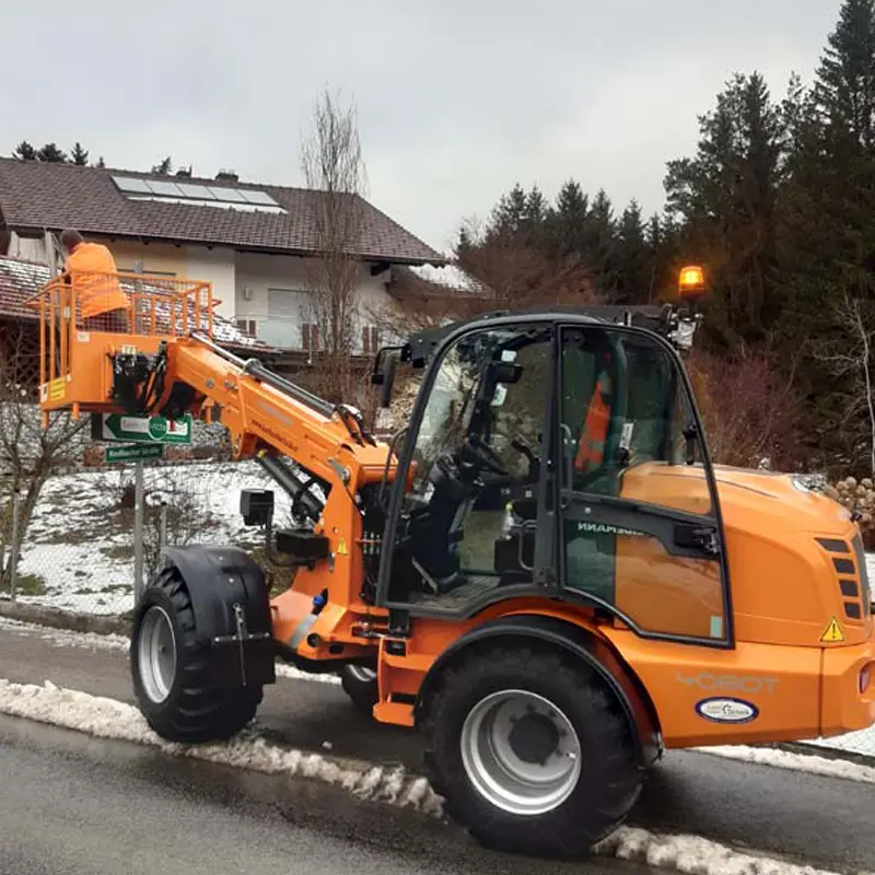 Orangefarbener Teleskoplader WM 4080T vor einem schneebedeckten Haus, eine Person steht in einer angehobenen Arbeitsbühne.