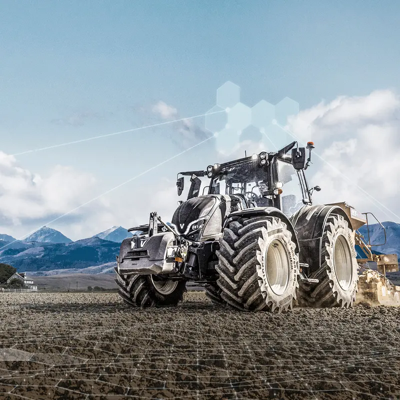 Valtra Traktor arbeitet auf einem Feld vor einer Bergkulisse unter bewölktem Himmel.