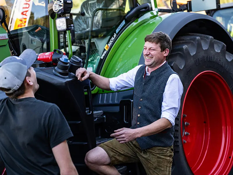 Két férfi nevetve áll egy Fendt traktor előtt