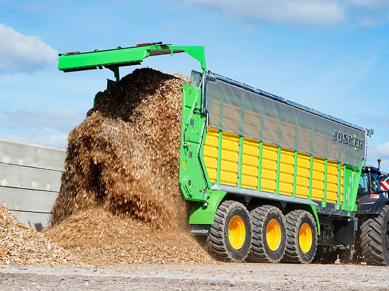 Remorca de transport Joskin aruncă așchii de lemn lateral prin intermediul unei clapete hidraulice în peretele înalt al silozului