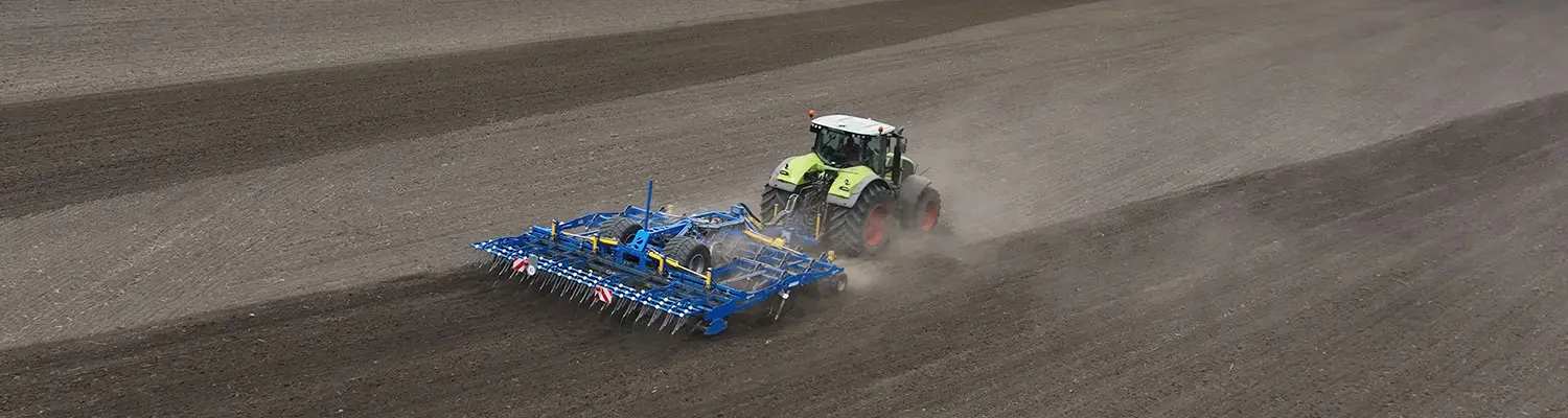Un tractor trage o unealtă de prelucrare a solului Treffler Orgapic peste un câmp mare, situat pe un sol prăfuit.