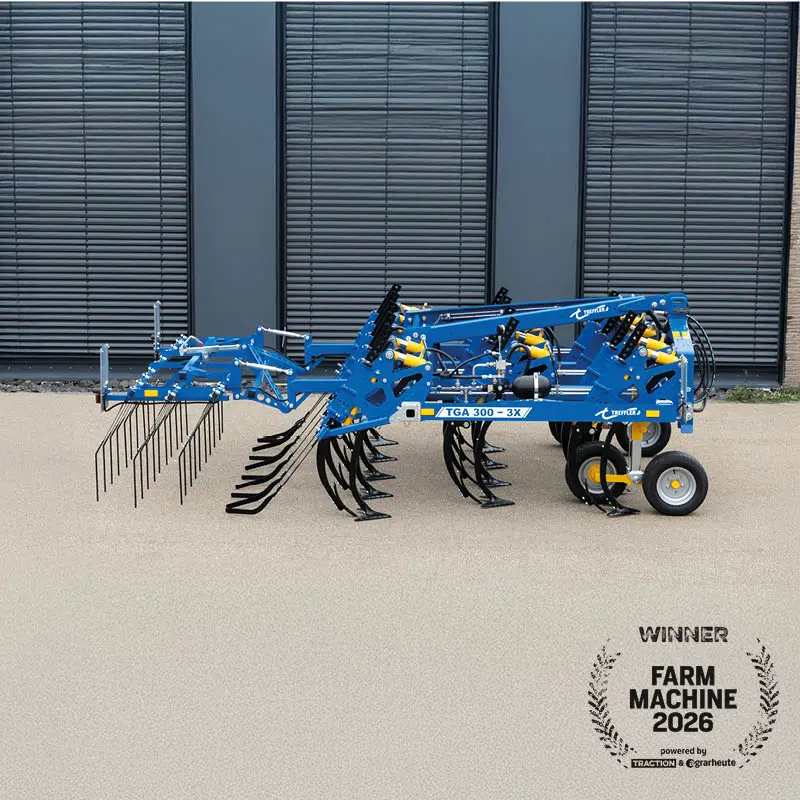 Blauer Treffler TGA 300‑3X Grubber mit Zinken und Rädern, seitlich vor Hallenfassade, Award-Logo „Farm Machine 2026“ unten rechts