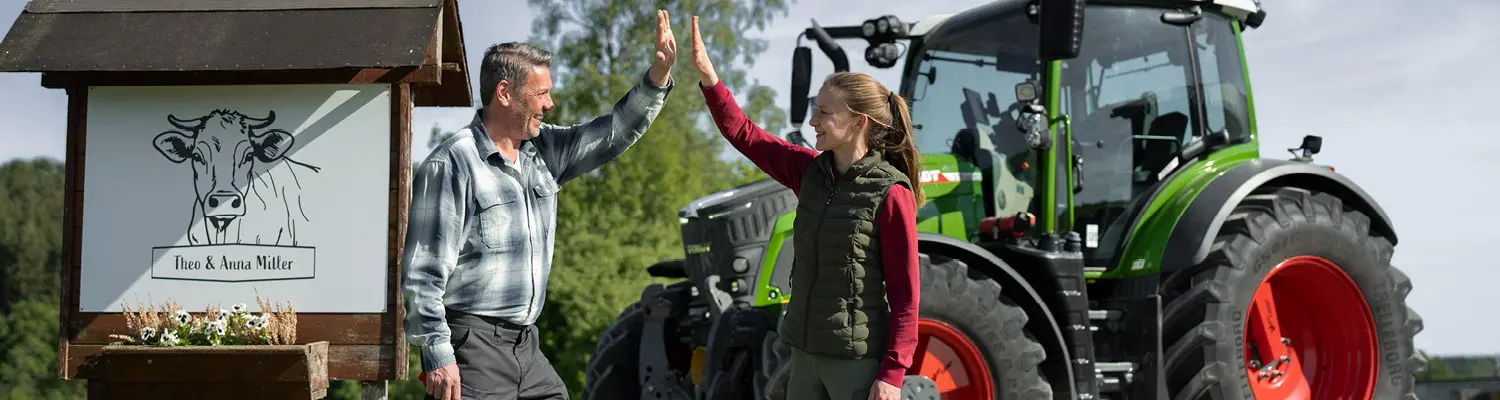 Headerbild Fendt Roadshow: Zwei Personen, ein Herr und eine Frau stehen vor einem Fendt 500 Vario und geben einander ein high-five.