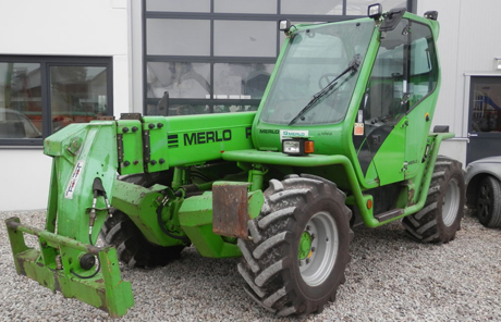 Grüner Merlo-Teleskoplader vor einem Gebäude.