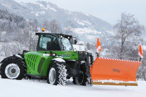 Grüner Merlo-Multifarmer mit Schneepflug im verschneiten Gebirge.