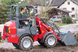 Un uomo sta guidando un trattore Weidemann 1160 Hoftrac in una proprietà rurale.