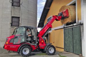 Mann fährt einen roten Weidemann Teleskoplader 2080T und transportiert Heuballen.