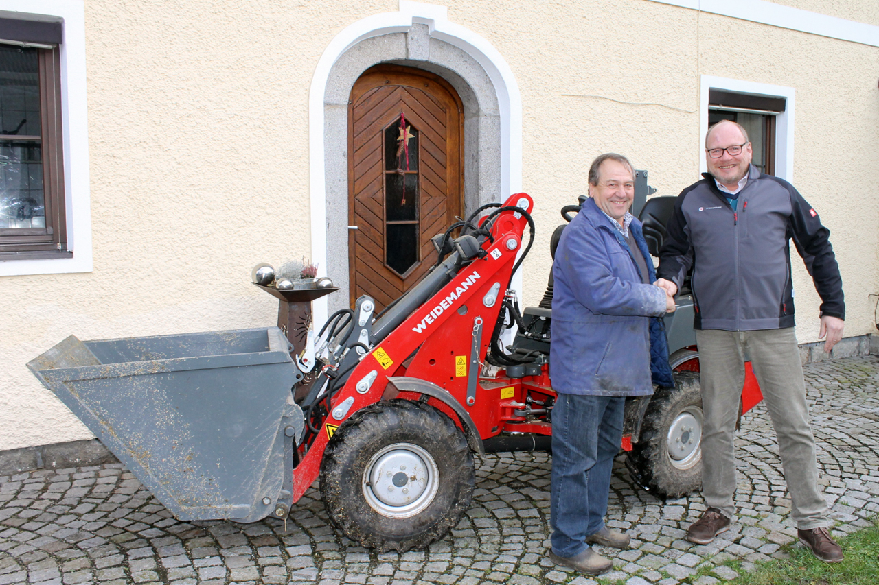 Zwei Männer schütteln sich vor einem roten Weidemann Radlader die Hand.