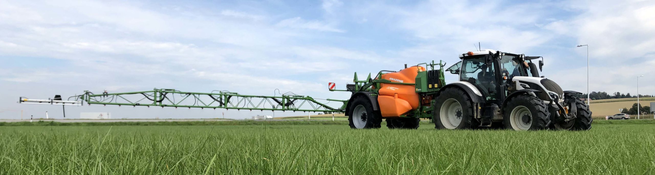 Ein Traktor mit Amazone-Spritzgerät fährt über ein grünes Feld.