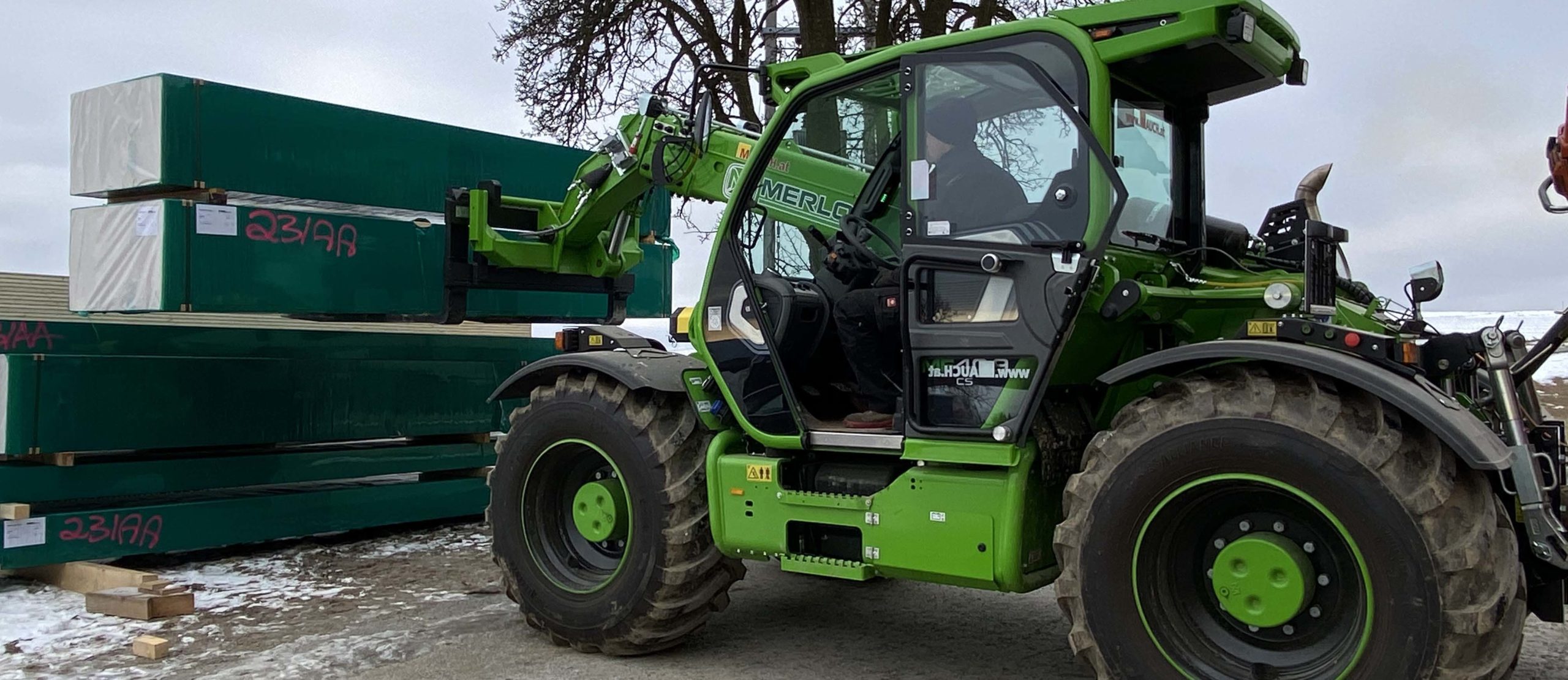 Ein grüner Merlo-Gabelstapler hebt grüne Paletten im Freien.