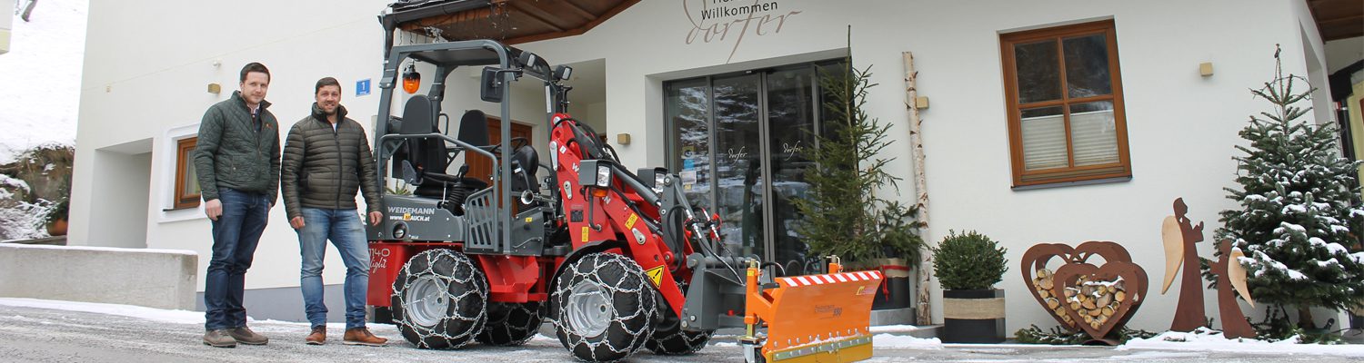 Zwei Männer stehen neben einem Weidemann-Radlader vor dem Hotel Dorfer.