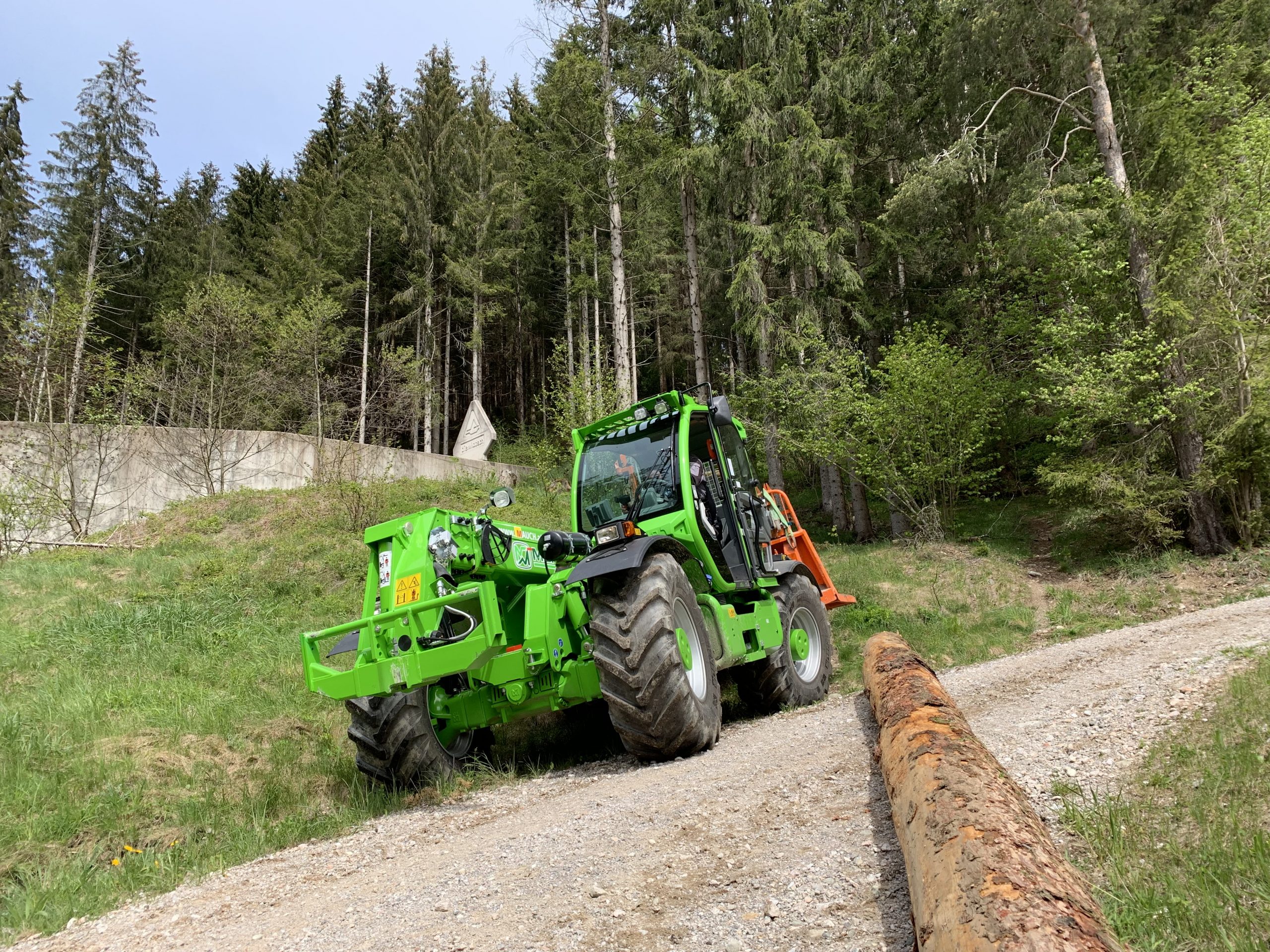 Ein grün lackierter Multifarmer zieht einen Baumstamm auf einem Waldweg.