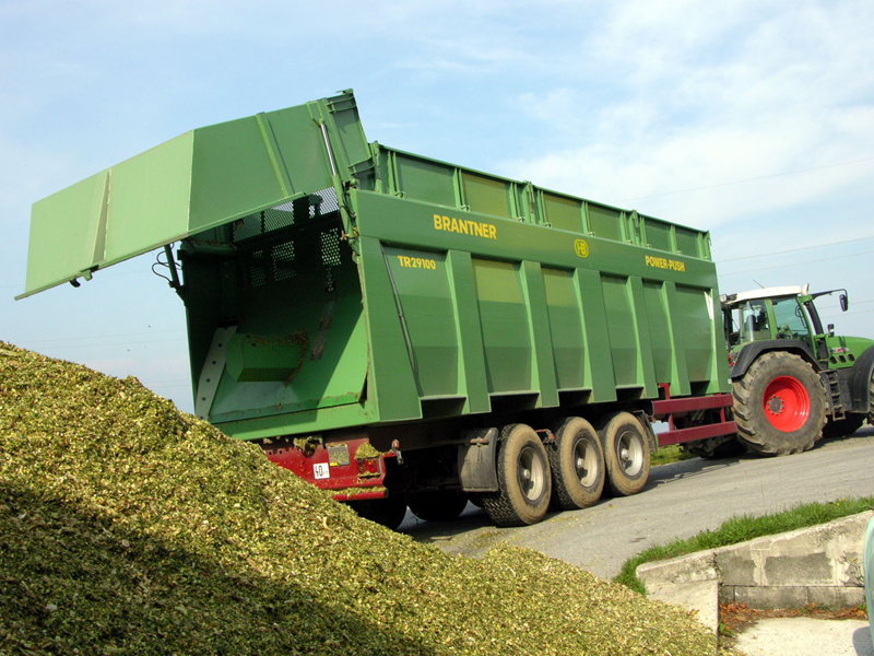 Ein grüner BRANTNER Abschiebewagen TR29100 wird von einem Traktor entladen.