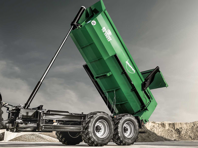 Grüner Kipperanhänger von Fliegl in halb hochgeklappter Position auf einer Baustelle.