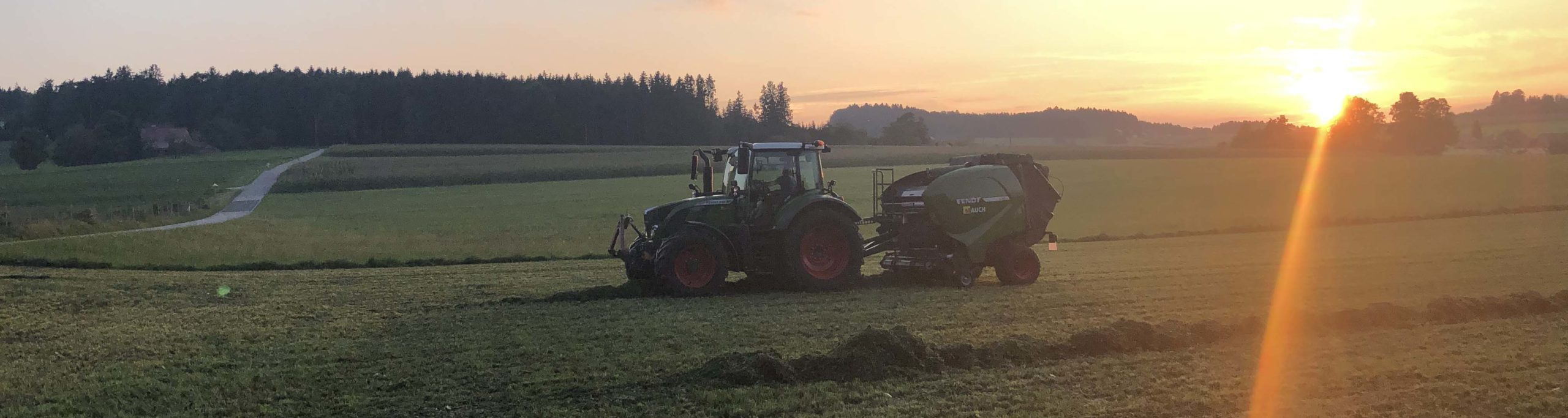 Traktor der Marke Fendt auf einem Feld bei Sonnenuntergang.