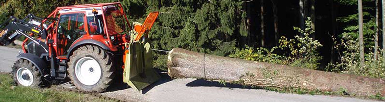Traktor zieht mit einem Holzknecht Werkzeug einen Baumstamm entlang einer Straße.