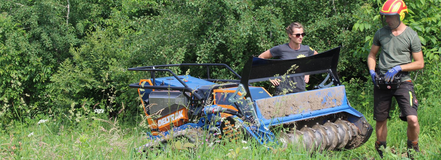 Zwei Männer demonstrieren ein Irus Deltrak Fahrzeug auf einer Wiese.