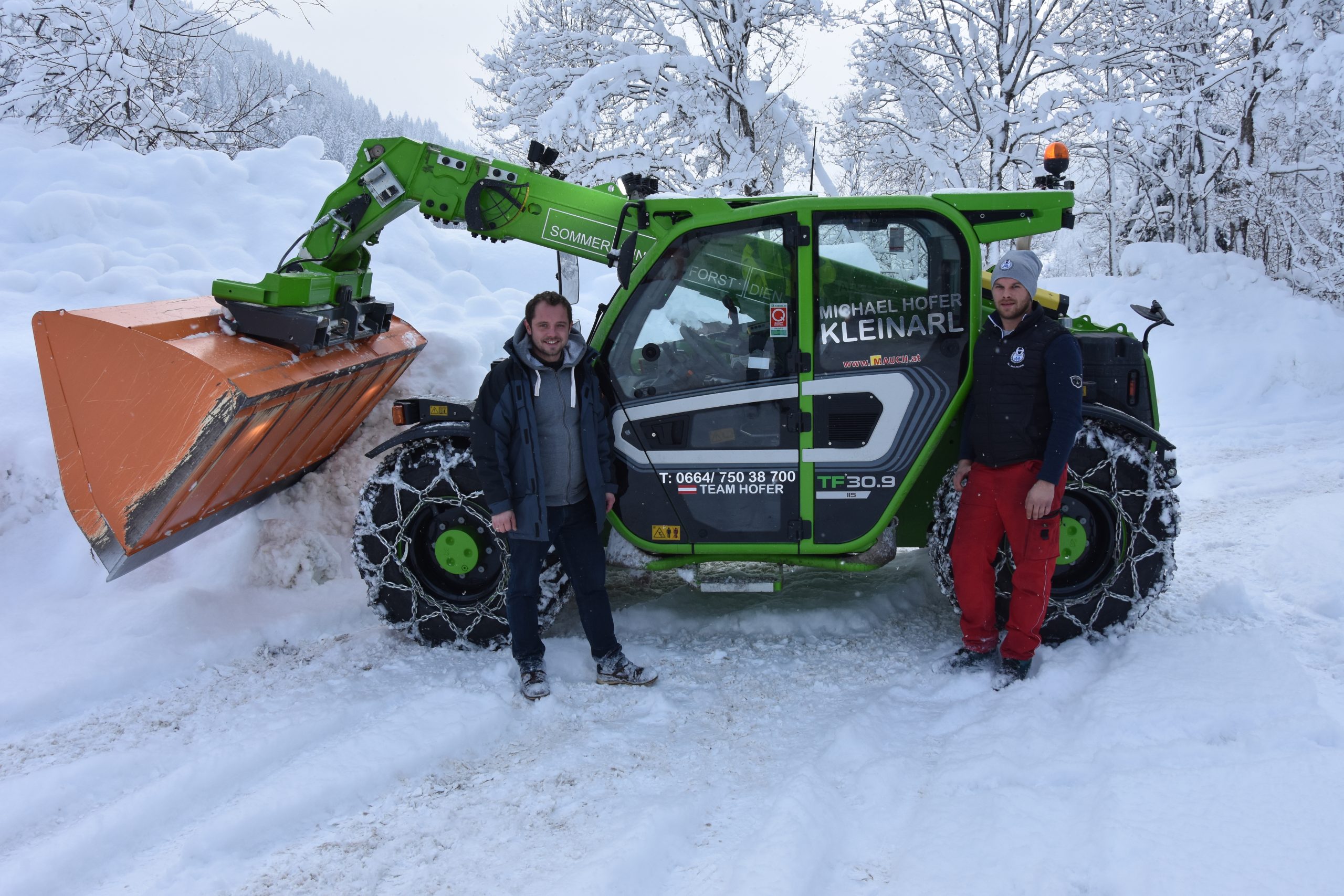 Zwei Männer stehen vor einem grünen Merlo TF30.9 Schneeräumfahrzeug im Schnee.