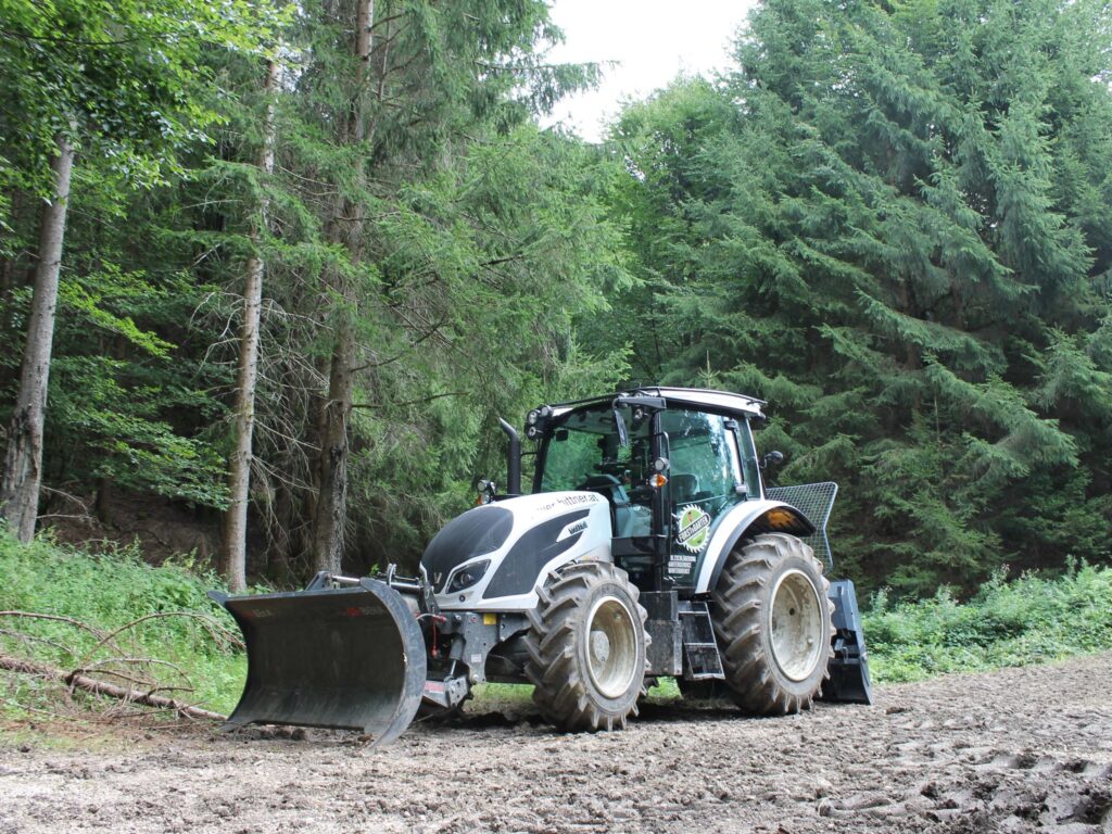 Tractor cu lopată conduce de-a lungul unei poteci forestiere.