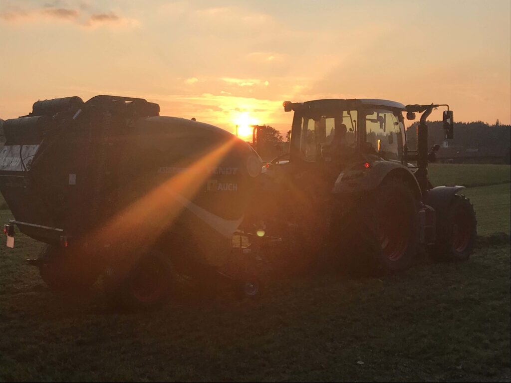 Traktor Fendt i prikolica Mauch na polju u zalazak sunca.