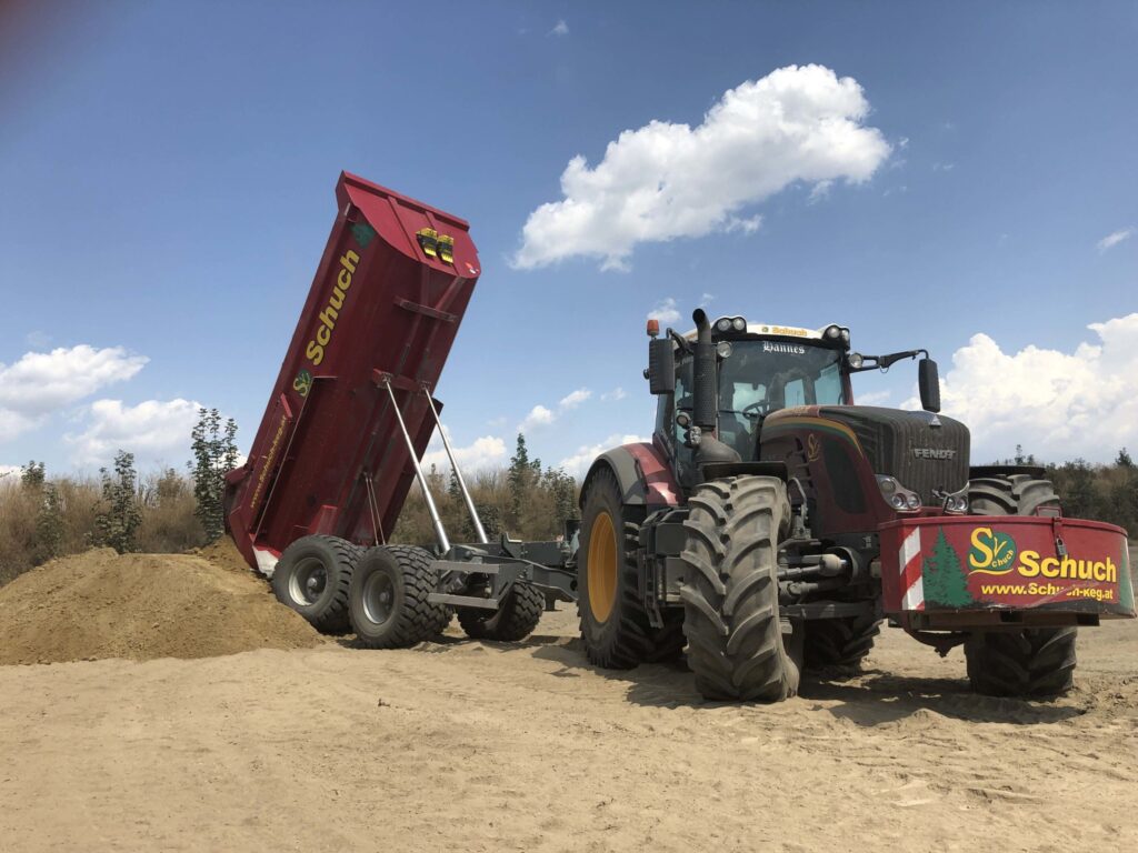 Un tractor Fendt roșu cu o remorcă Schuch aruncă nisip pe un șantier.