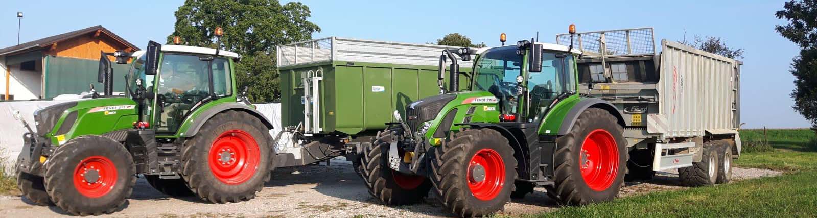 Zwei grüne Fendt-Traktoren stehen mit Anhängern auf einem Bauernhof.