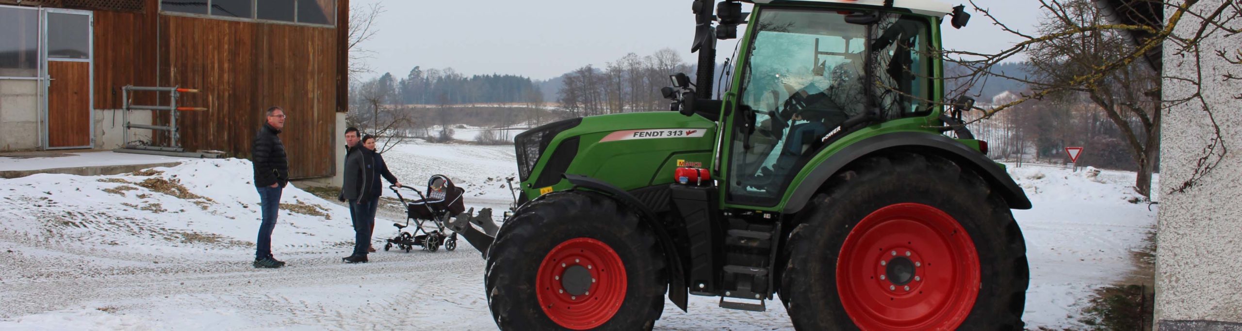 Traktor Fendt 313 Vario vor einem verschneiten Bauernhof, drei Personen daneben.