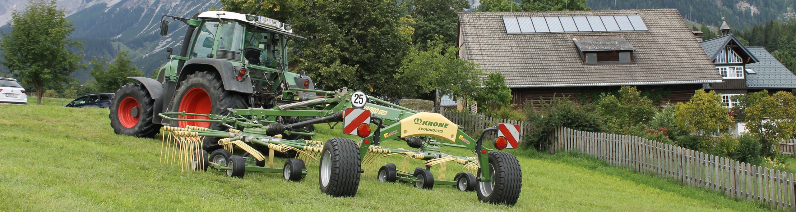 Traktor mit Krone Swadro-Maschine vor einem Haus in ländlicher Umgebung.