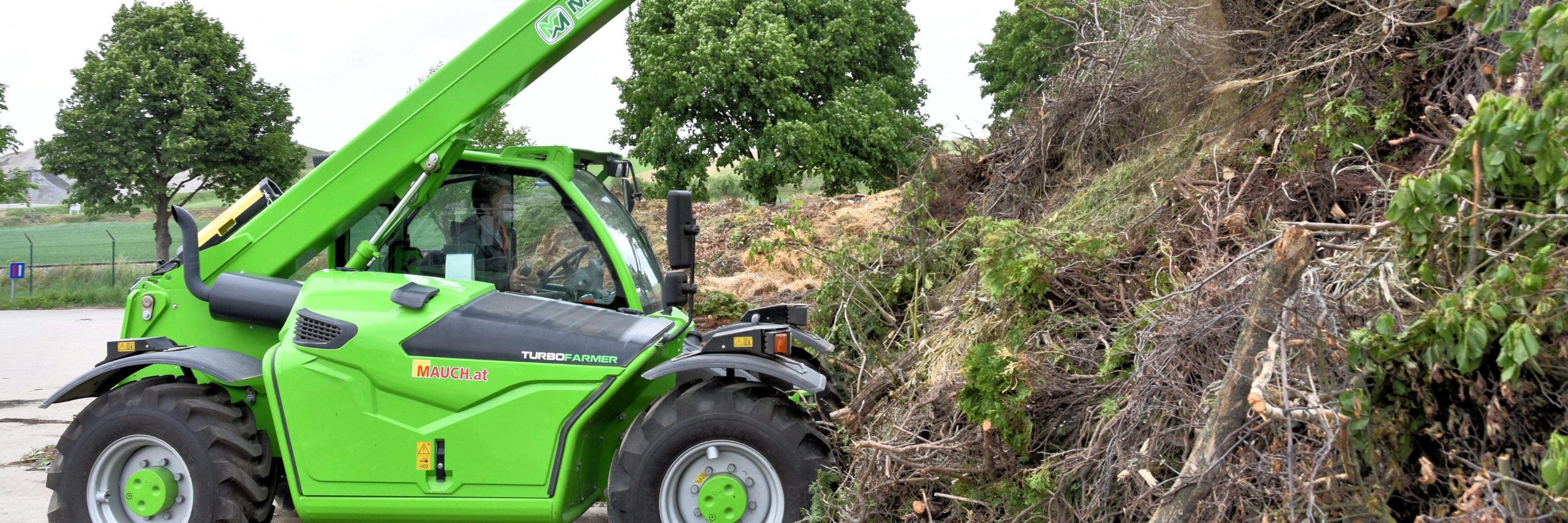 Grüner Merlo TurboFarmer TF35 Hebelader bei der Arbeit, im Hintergrund Bäume und ein Zaun.