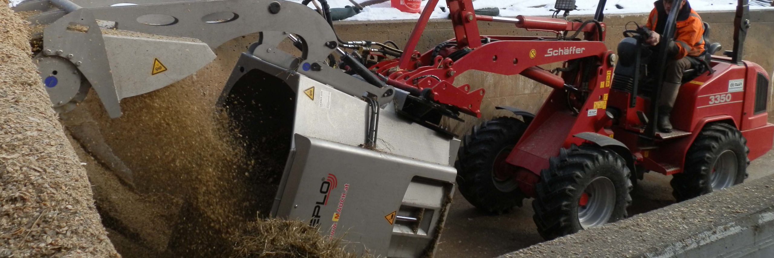 Ein roter Schäffer 3350 Lader mit einem Sieplo-Anbaugerät bewegt Stroh in einem Gehege.