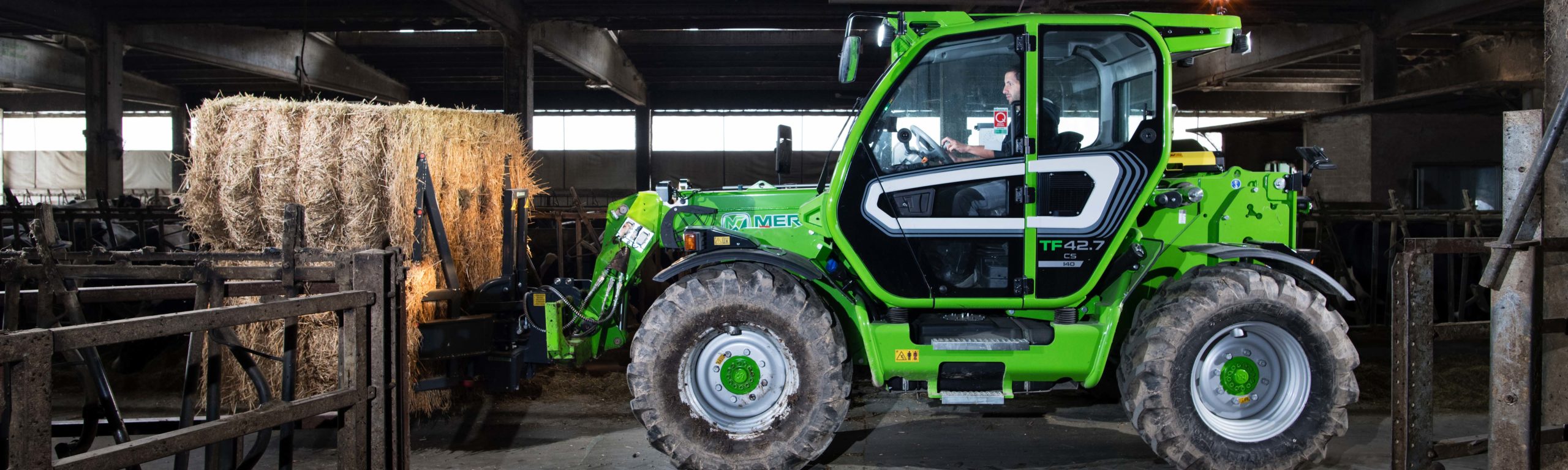 Merlo TF42.7 hebt eine große Rundballen Heu in einem Stall.