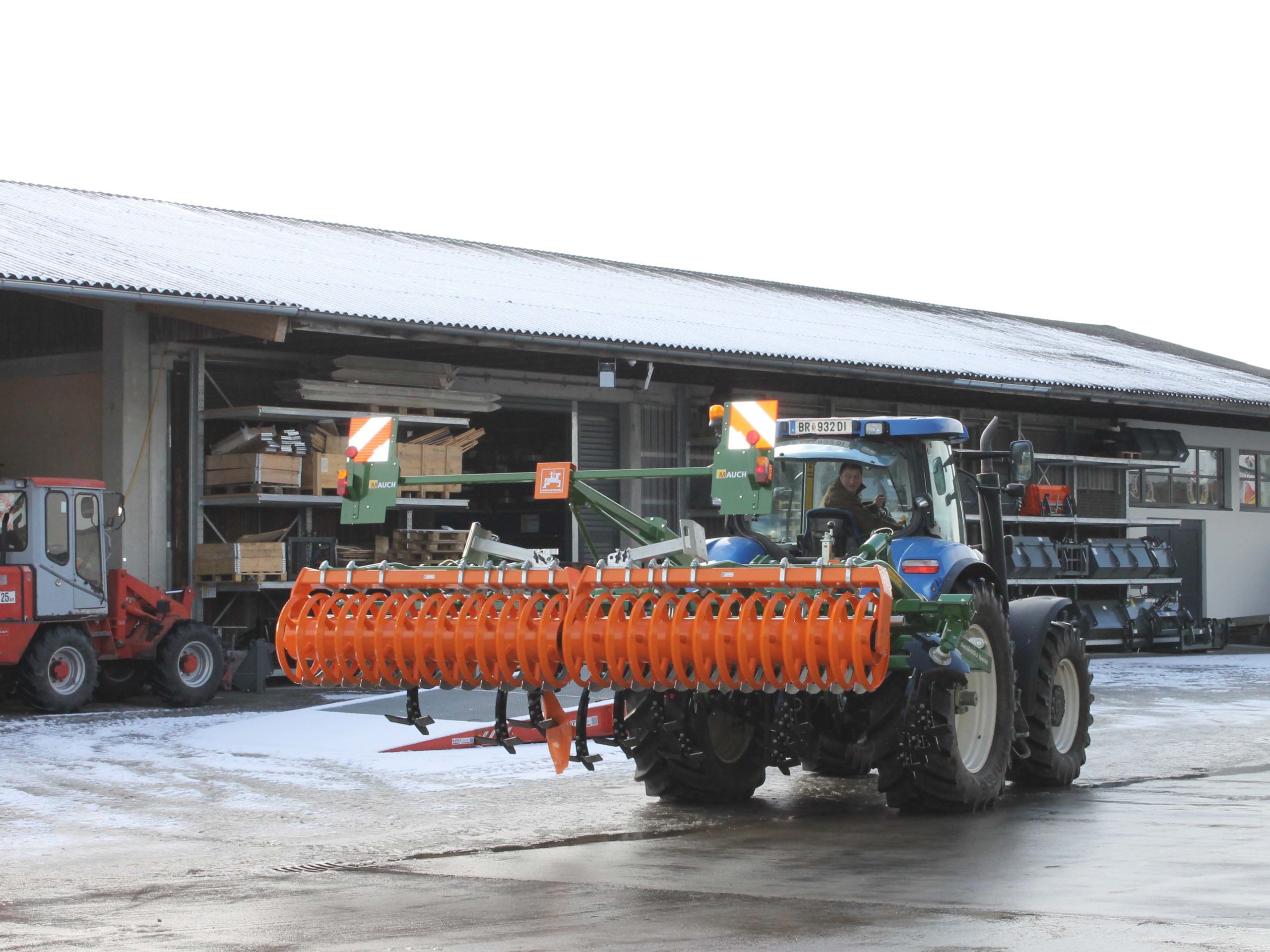 Traktor mit Amazone Cenius-Anbaugerät vor einem Lagergebäude.