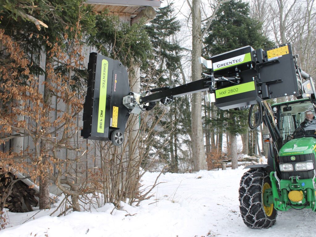 Traktor mit Greentec-Heckenmulcher HXF 2802 schneidet Hecken im winterlichen Wald.