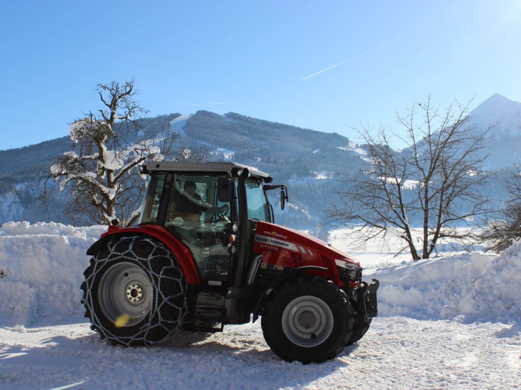 Roter Massey Ferguson 5710 SL Traktor mit Schneeketten im verschneiten Alpenhintergrund.