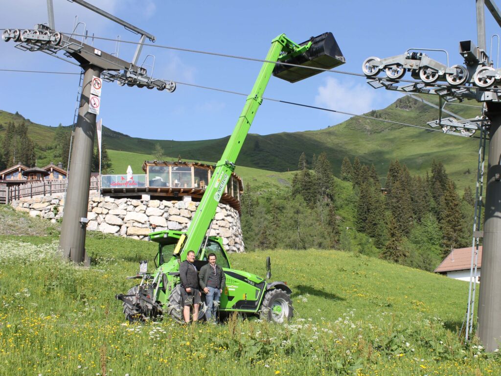 Zwei Männer stehen neben einem grünen Merlo Hubsteiger in einer Berglandschaft.