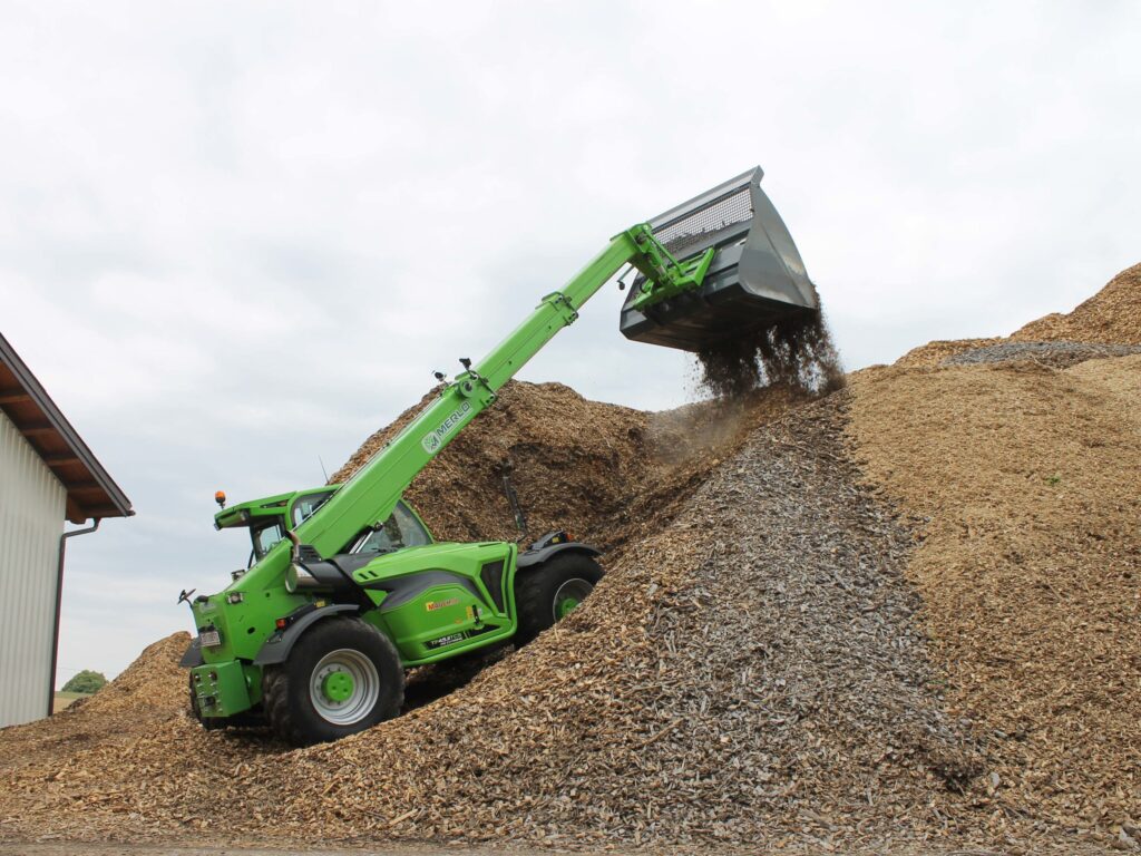 Ein grüner Merlo 45.11 Teleskoplader schüttet Holzschnitzel auf einen großen Haufen.